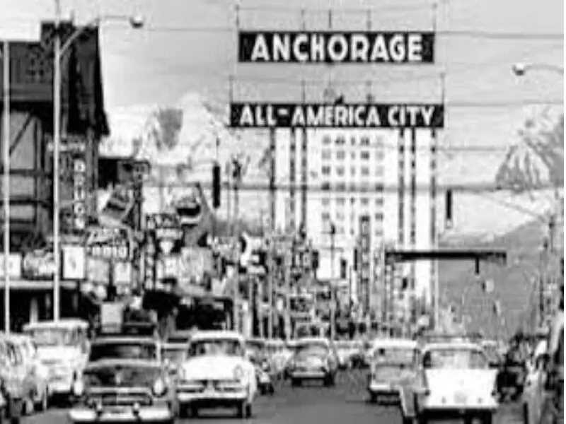 A black and white photo of cars driving down the street.