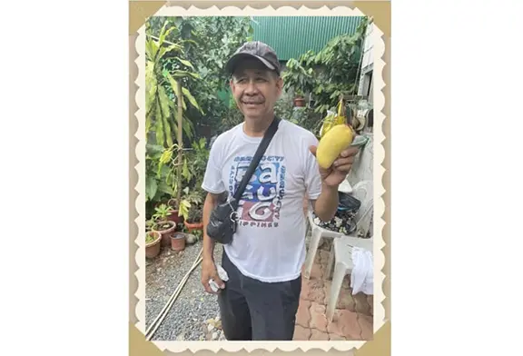 Man holding a mango in a garden.