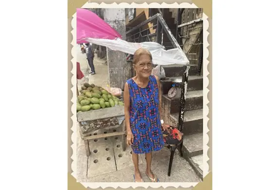 Elderly woman standing by fruit stall.