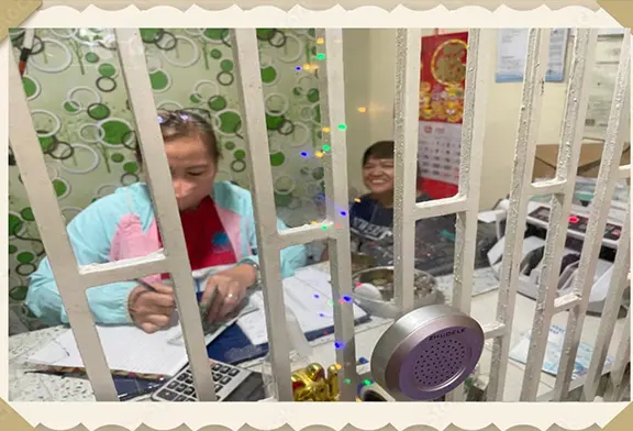 Two women working behind a barred counter.