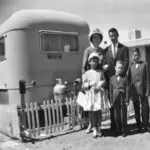 Family posing in front of a vintage trailer.