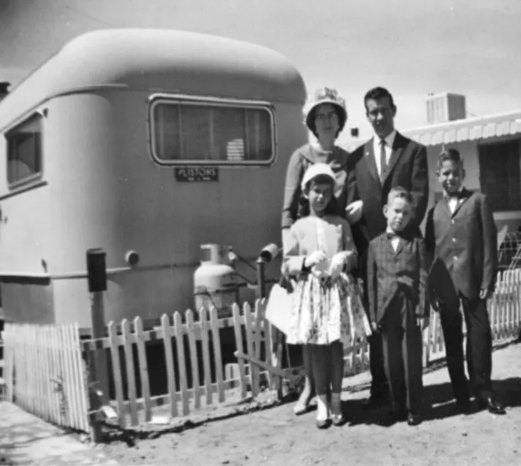 Family posing in front of a vintage trailer.